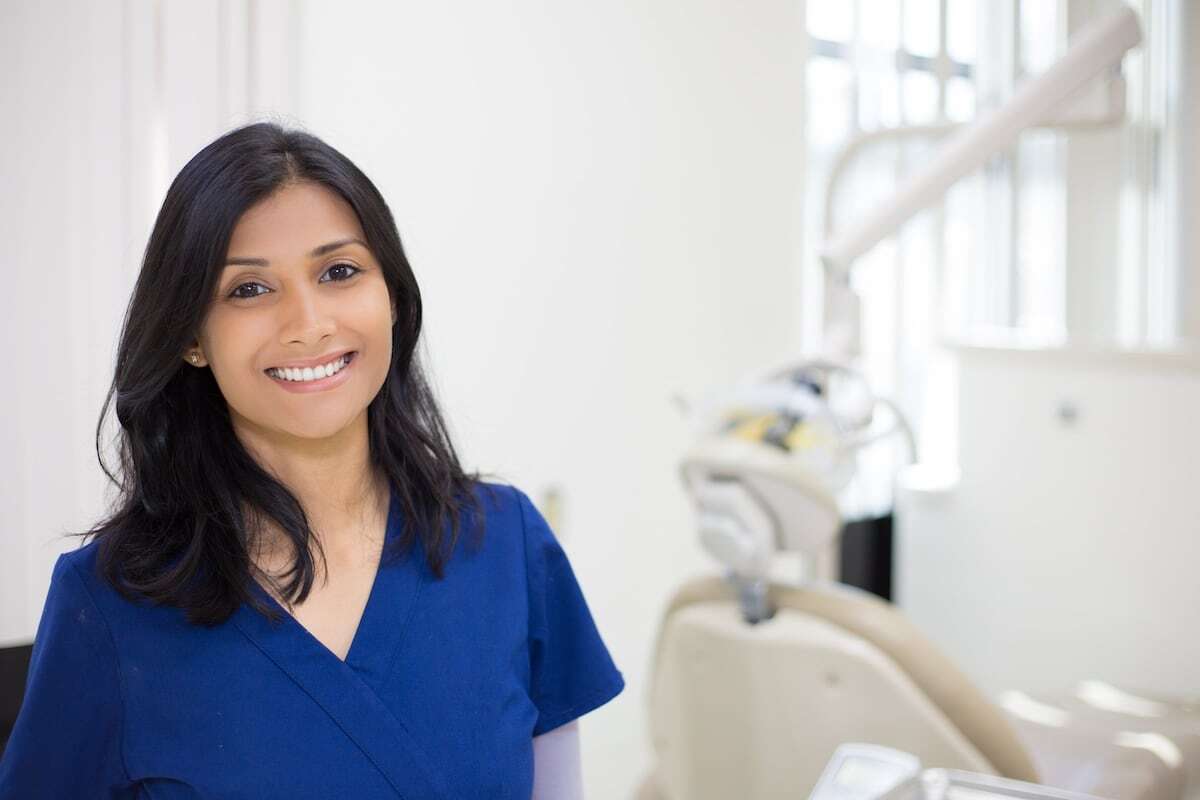a woman smiling at the camera, next to a dental examination chair